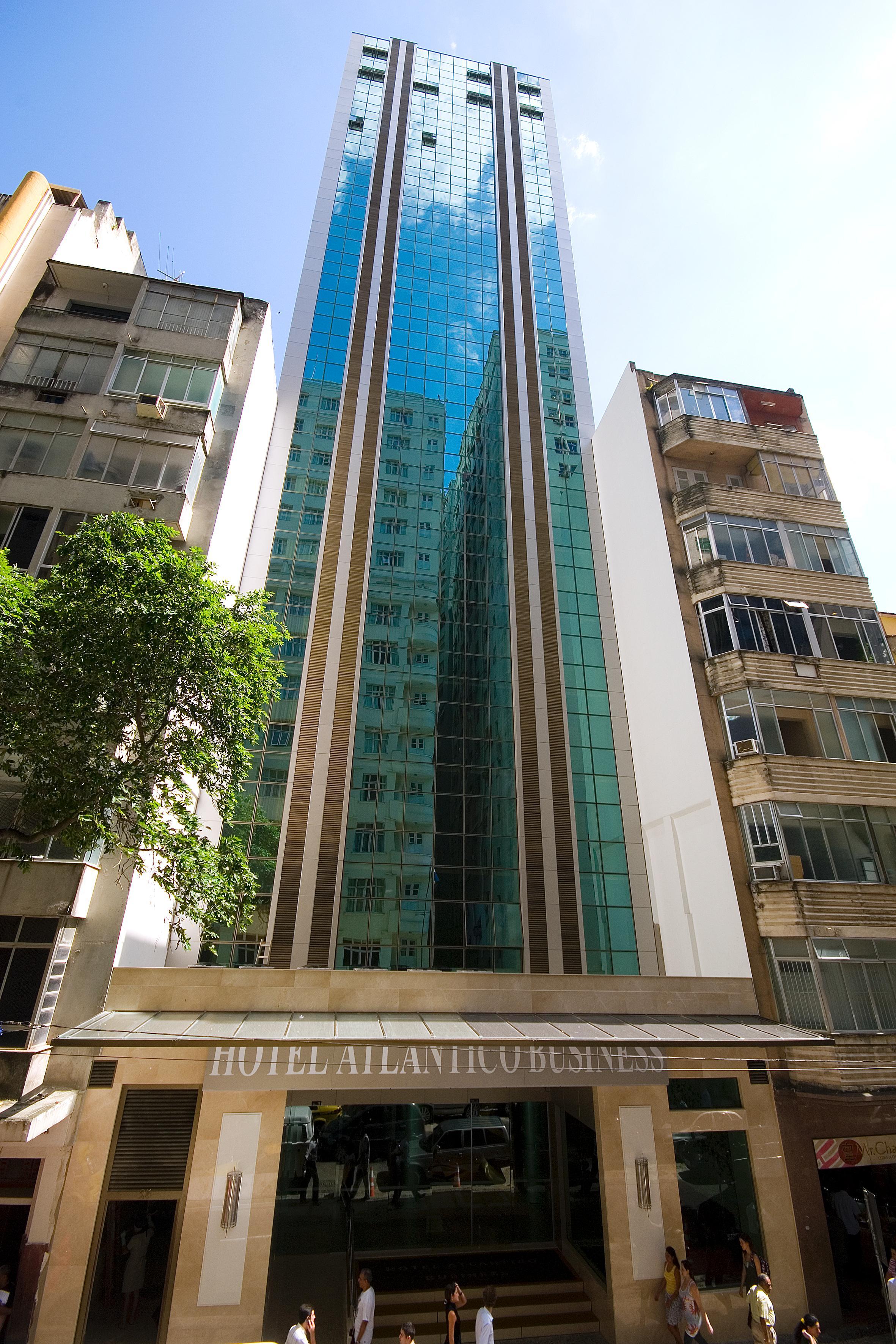 Hotel Atlântico Business Centro Río de Janeiro Exterior foto The photo shows a modern multi-story building with a sleek glass facade. The building appears to have several floors with large windows, reflecting sunlight, and is flanked by a tree on one side and an older, more traditional residential structure on